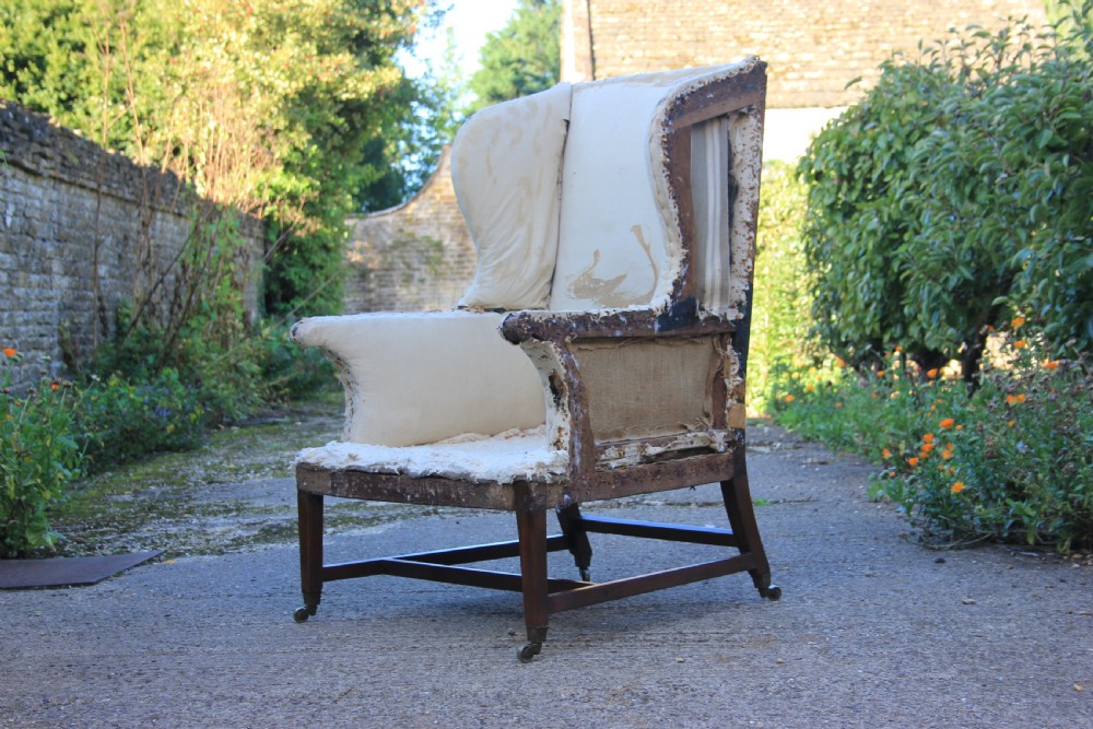 An early 18th-century wingback armchair featuring a dark timber frame, prominent side wings, and worn beige calico upholstery. View IV