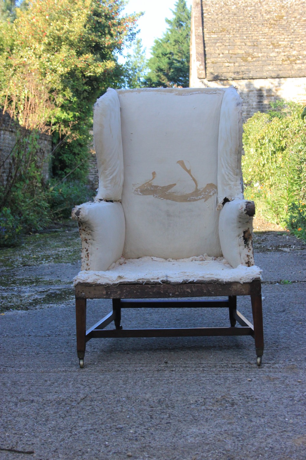 An early 18th-century wingback armchair featuring a dark timber frame, prominent side wings, and worn beige calico upholstery. View VI