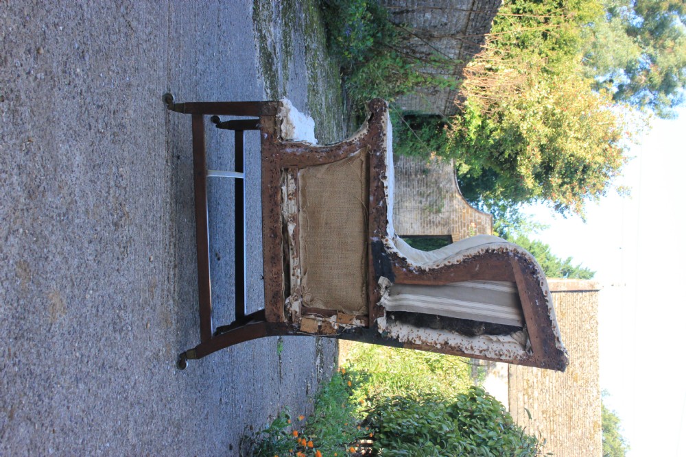 An early 18th-century wingback armchair featuring a dark timber frame, prominent side wings, and worn beige calico upholstery. View VII