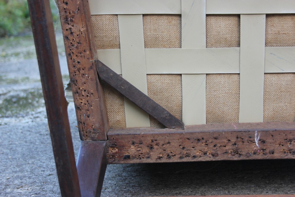 An early 18th-century wingback armchair featuring a dark timber frame, prominent side wings, and worn beige calico upholstery. View XI