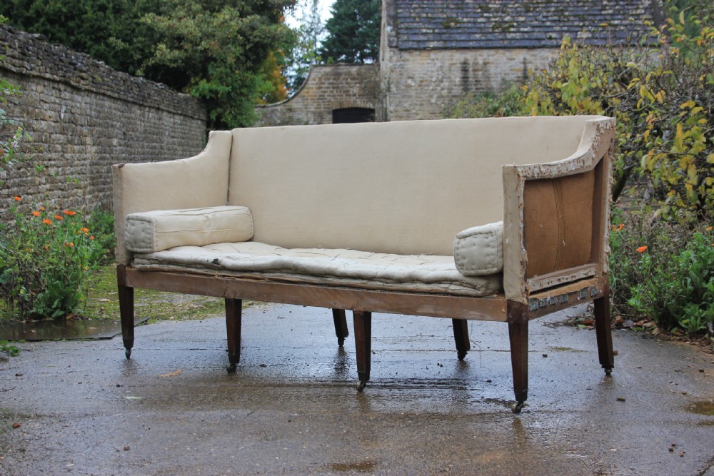 An early 19th-century sofa frame with calico lining, cylindrical bolster cushions, and square mahogany legs on brass castors.