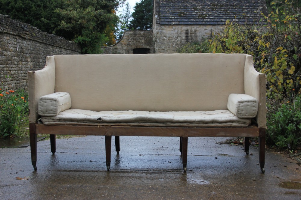 An early 19th-century sofa frame with calico lining, cylindrical bolster cushions, and square mahogany legs on brass castors. View II