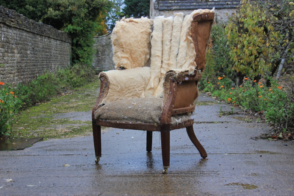 A stripped Georgian barrel back armchair frame showing horsehair padding, a curved backrest, and mahogany legs with brass castors.