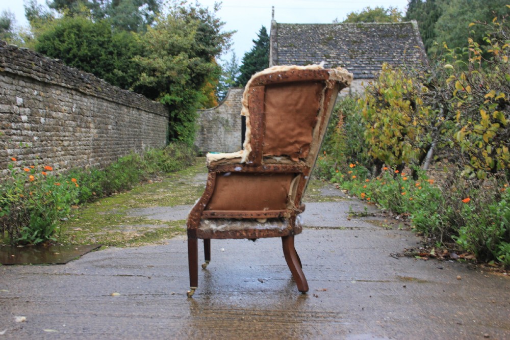 A stripped Georgian barrel back armchair frame showing horsehair padding, a curved backrest, and mahogany legs with brass castors. View II