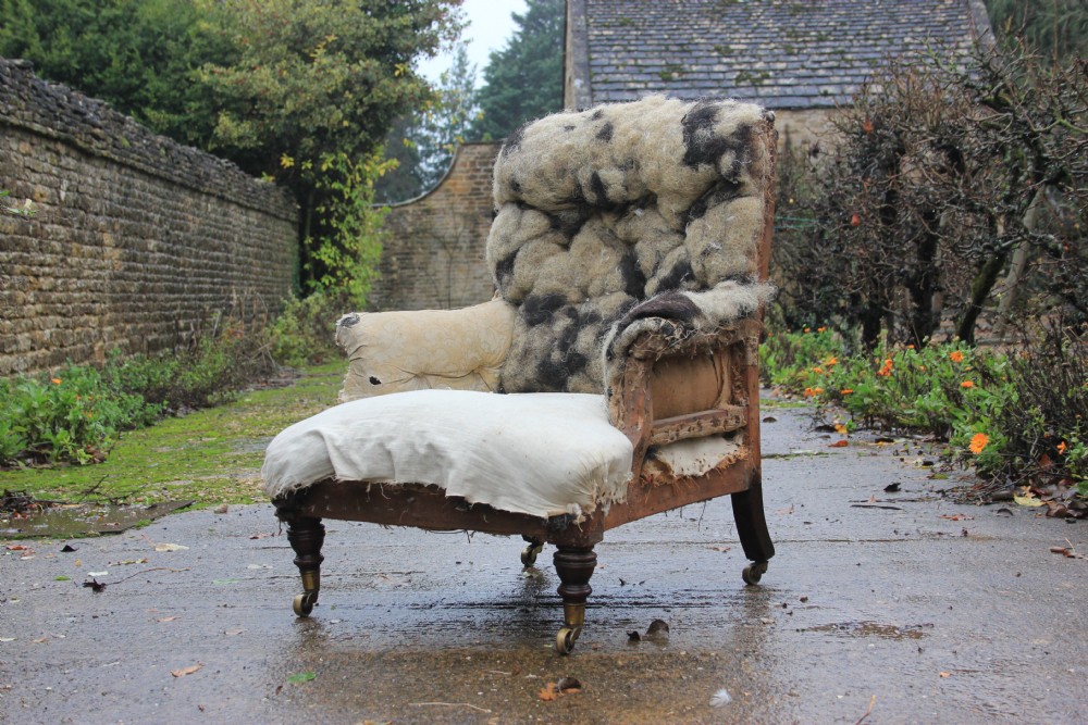 An antique Victorian Howard and Sons armchair frame featuring exposed horsehair padding, turned front legs with brass castors, and splayed back legs.