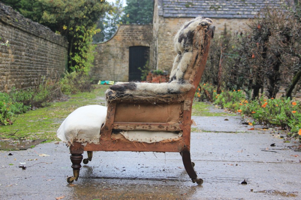 An antique Victorian Howard and Sons armchair frame featuring exposed horsehair padding, turned front legs with brass castors, and splayed back legs. View II