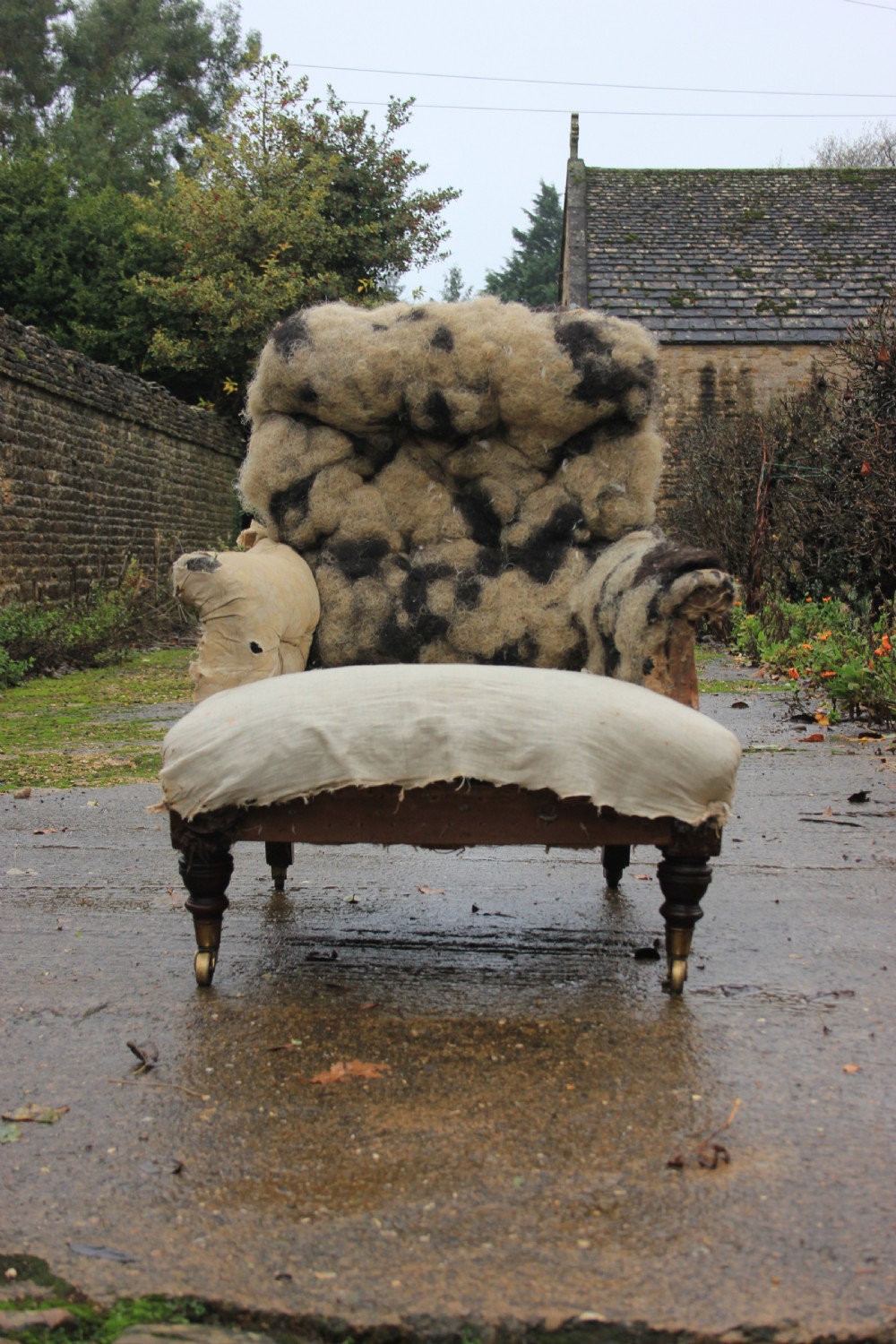 An antique Victorian Howard and Sons armchair frame featuring exposed horsehair padding, turned front legs with brass castors, and splayed back legs. View III