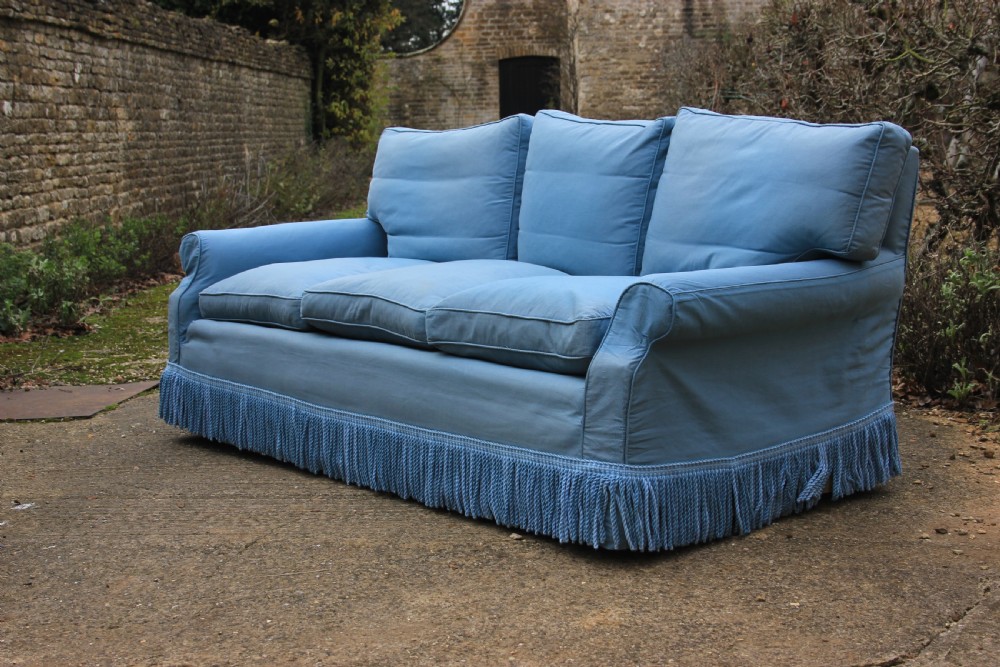 A three-seater English country house sofa upholstered in light blue fabric featuring a deep bullion fringe skirt.