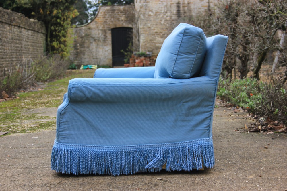 A three-seater English country house sofa upholstered in light blue fabric featuring a deep bullion fringe skirt. View III