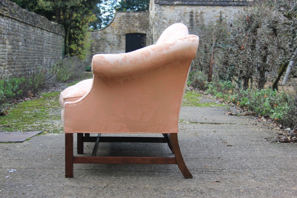 A peach damask upholstered camel back sofa featuring a serpentine seat cushion, out-scrolled arms, and square mahogany legs connected by stretchers. View V