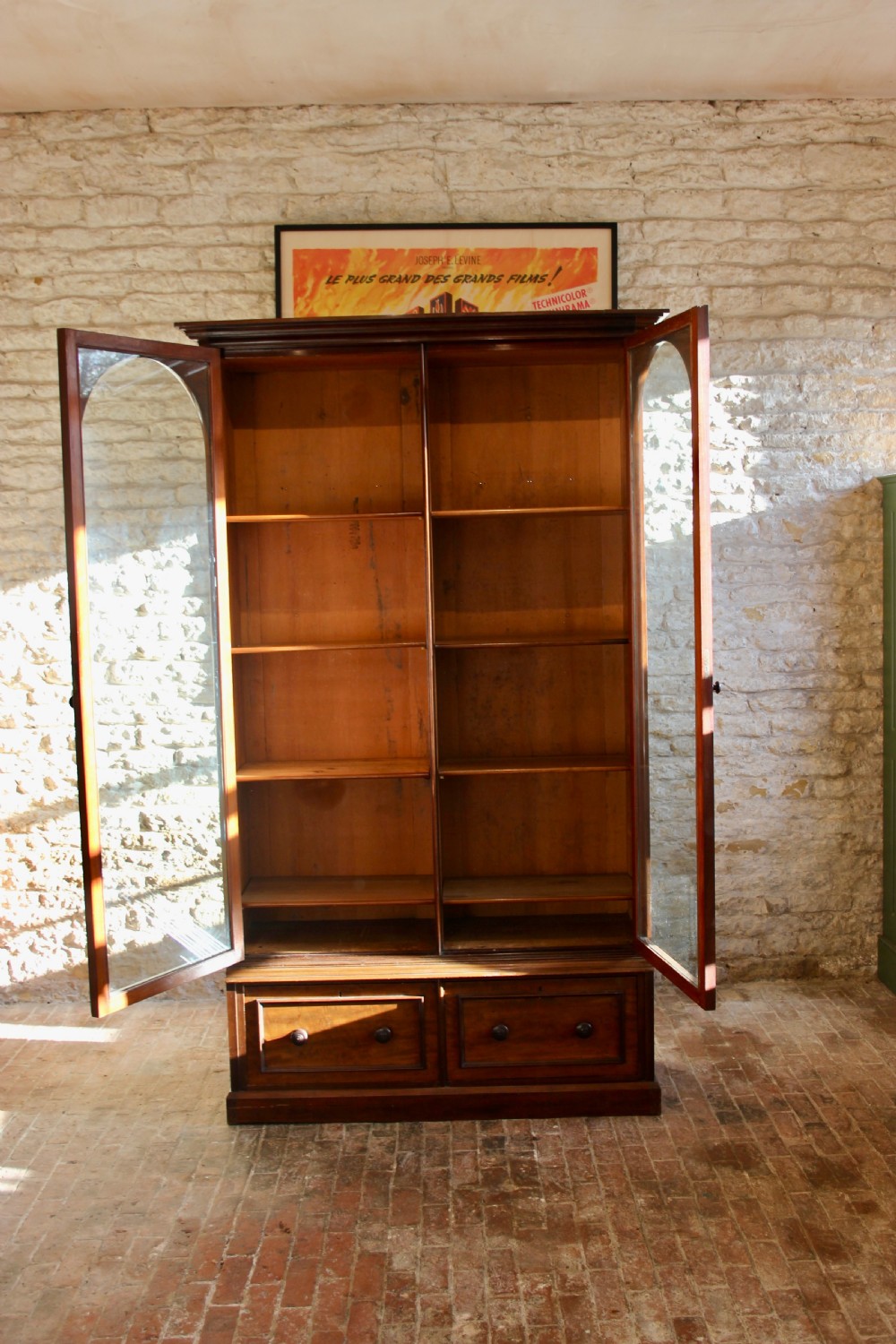 A 19th-century mahogany glazed bookcase featuring two arched glass doors, internal wooden shelving, and two lower drawers with turned wooden knobs. View V