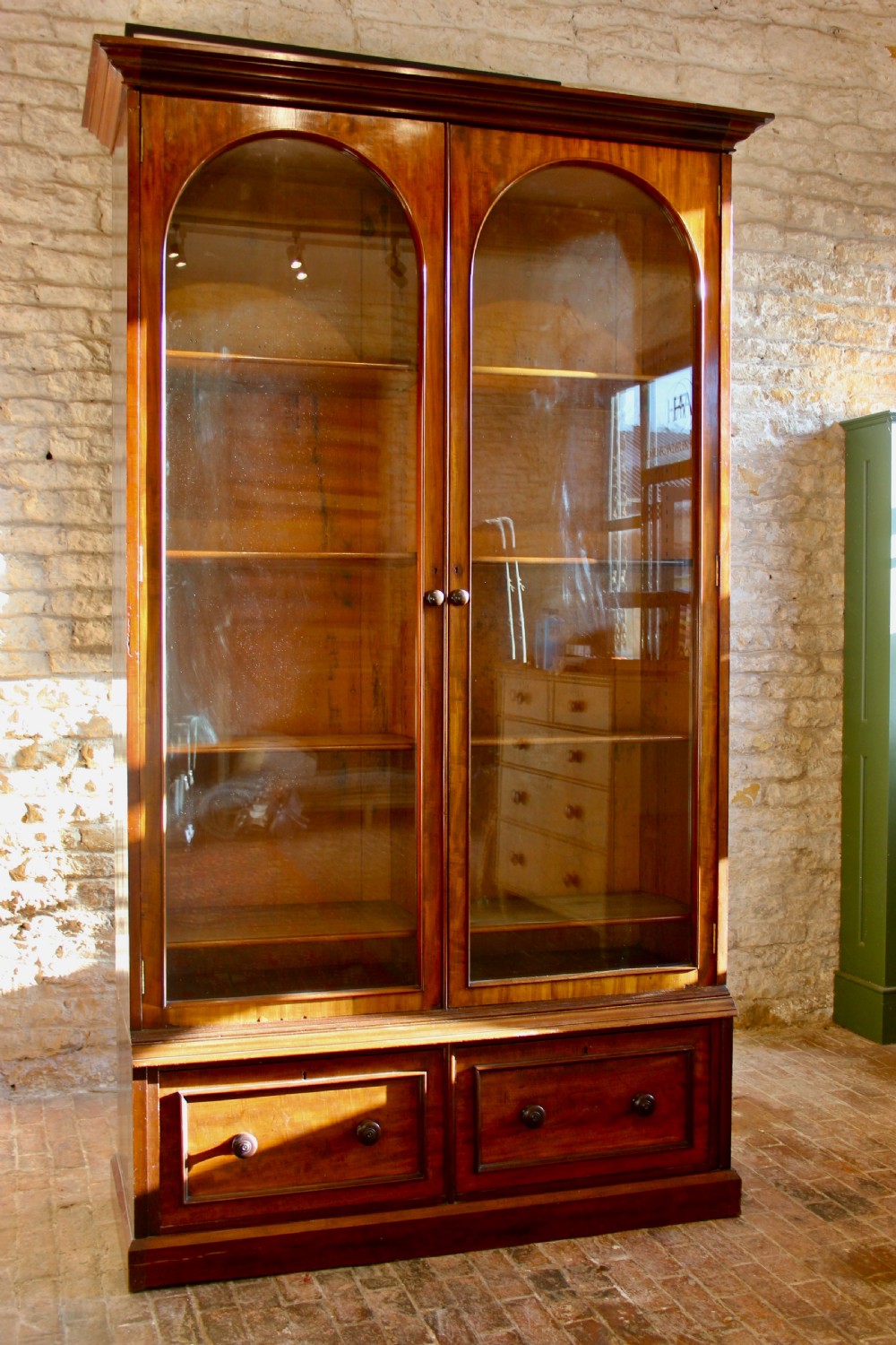 A 19th-century mahogany glazed bookcase featuring two arched glass doors, internal wooden shelving, and two lower drawers with turned wooden knobs. View VII
