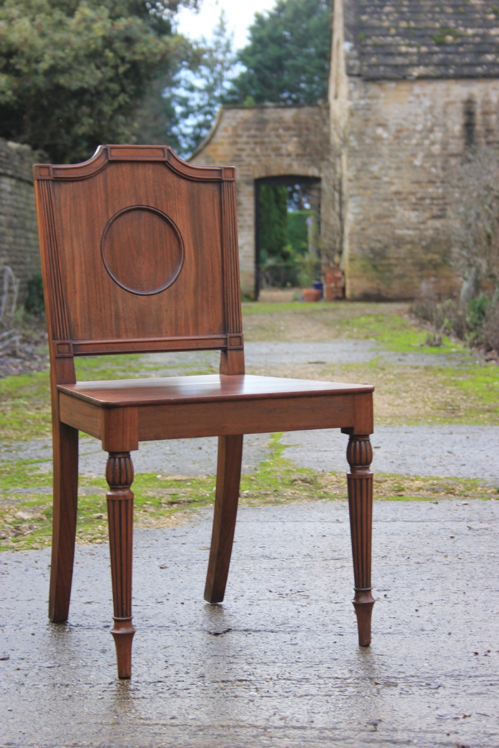 A pair of mahogany hall chairs featuring carved backrests with central circular mouldings, solid timber seats, and fluted turned front legs. View II