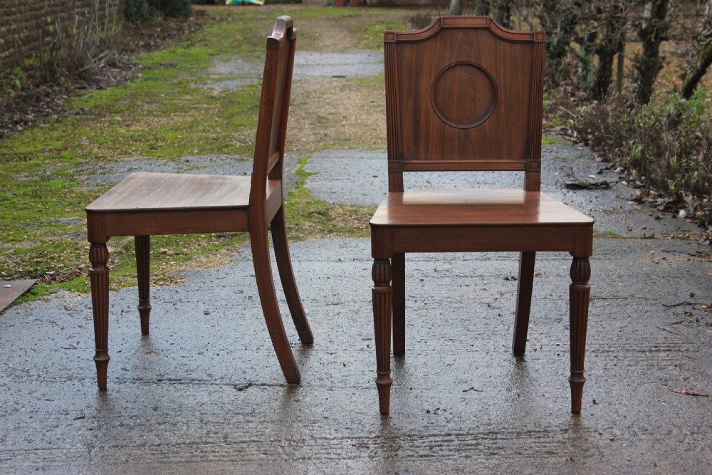 A pair of mahogany hall chairs featuring carved backrests with central circular mouldings, solid timber seats, and fluted turned front legs. View XI