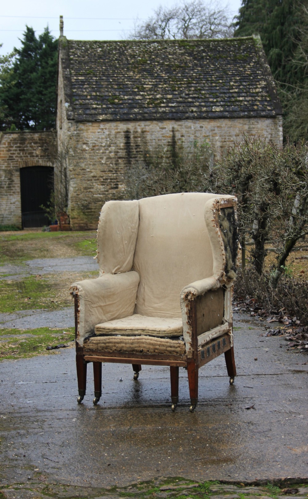 An early 19th century wingback armchair frame lined in neutral calico, featuring square tapered mahogany legs with brass castors.