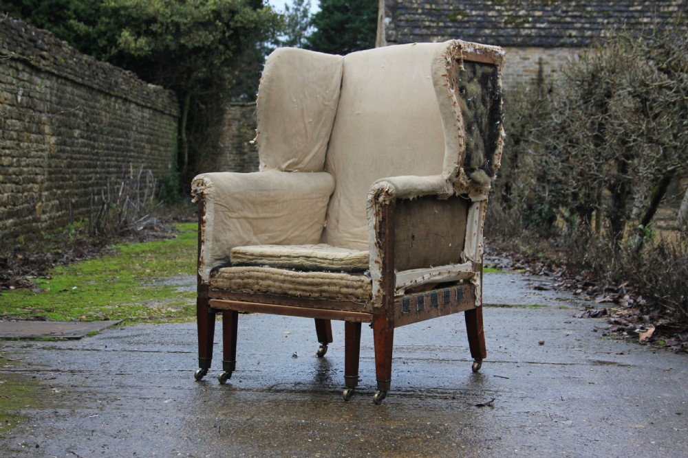 An early 19th century wingback armchair frame lined in neutral calico, featuring square tapered mahogany legs with brass castors. View II