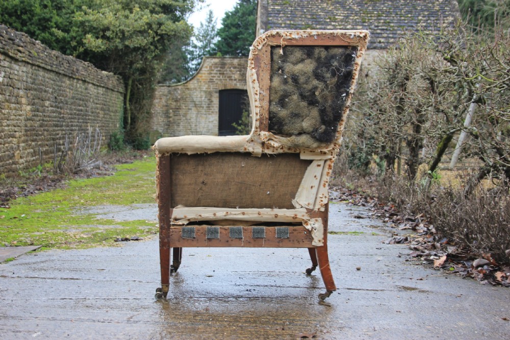 An early 19th century wingback armchair frame lined in neutral calico, featuring square tapered mahogany legs with brass castors. View V
