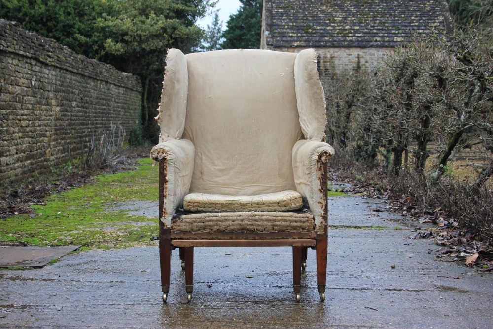 An early 19th century wingback armchair frame lined in neutral calico, featuring square tapered mahogany legs with brass castors. View VII
