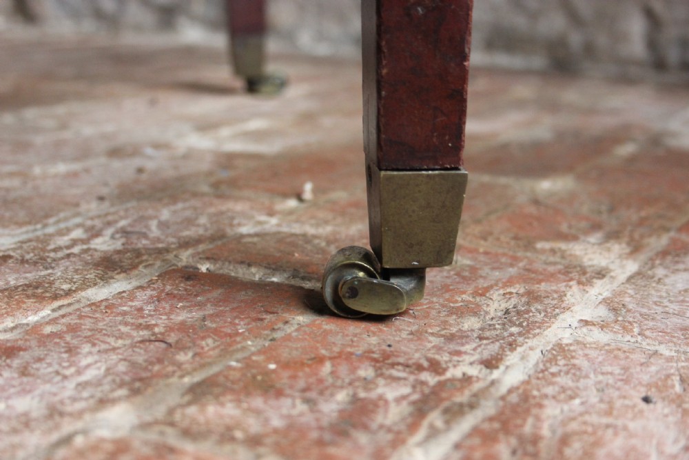 A square mahogany footstool frame with tapered legs and brass castors, showing exposed tacking rails where former upholstery was removed. View II