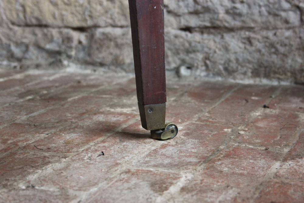 A square mahogany footstool frame with tapered legs and brass castors, showing exposed tacking rails where former upholstery was removed. View III