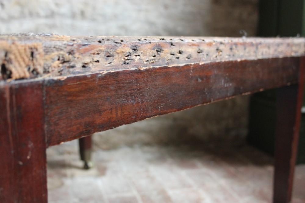 A square mahogany footstool frame with tapered legs and brass castors, showing exposed tacking rails where former upholstery was removed. View IV