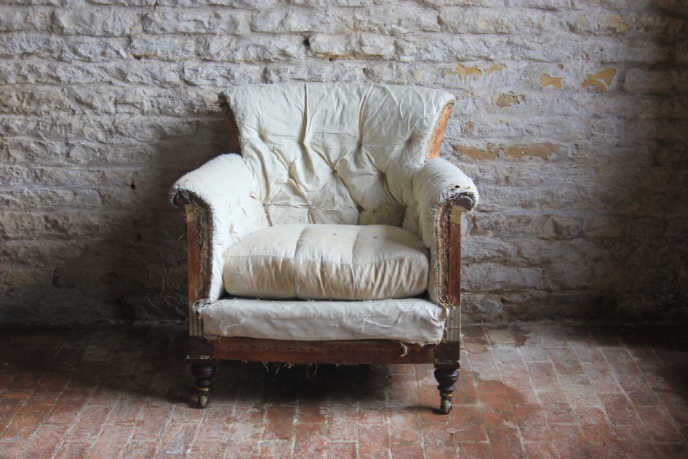 A Victorian Woodstock style armchair in calico under-upholstery featuring a buttoned back rest and turned front legs with brass castors.
