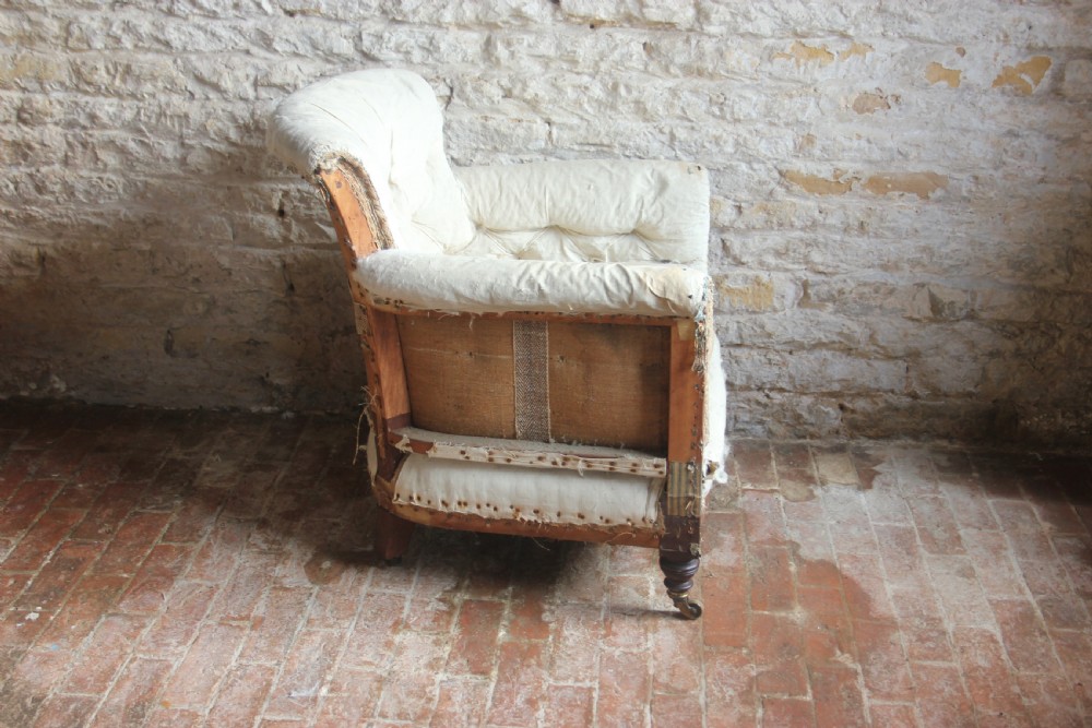 A Victorian Woodstock style armchair in calico under-upholstery featuring a buttoned back rest and turned front legs with brass castors. View II