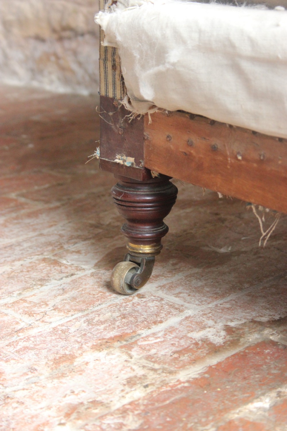 A Victorian Woodstock style armchair in calico under-upholstery featuring a buttoned back rest and turned front legs with brass castors. View III