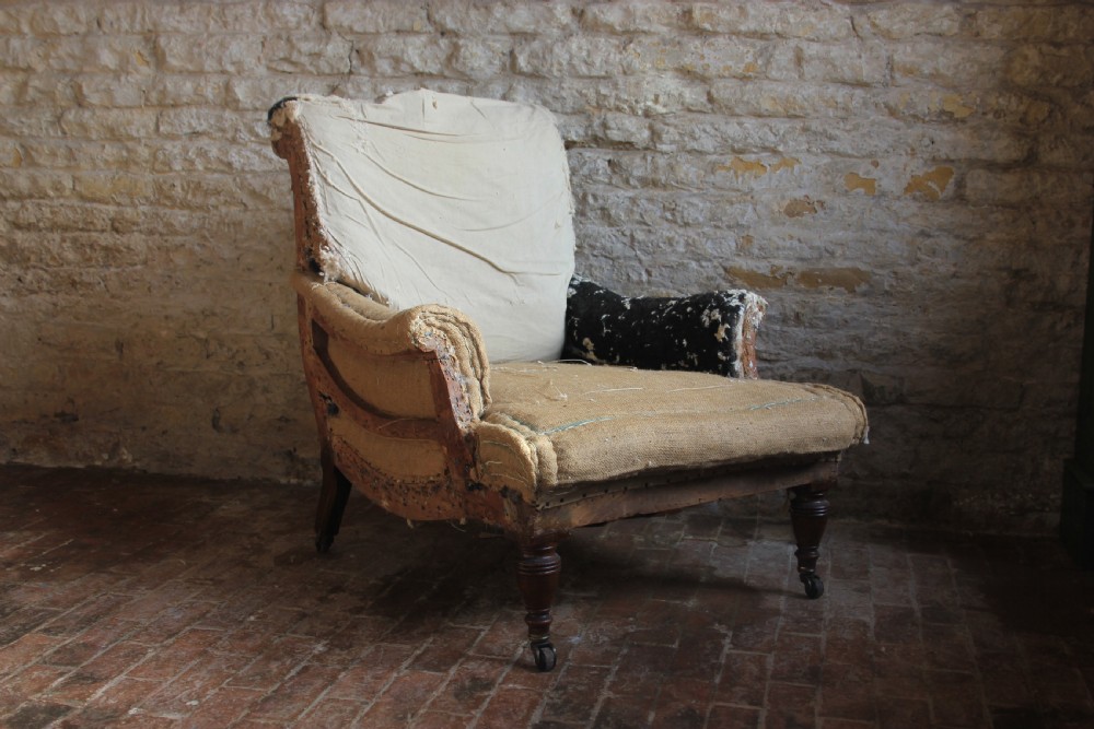 A Victorian deep-seated armchair frame with exposed calico and hessian sub-upholstery, featuring turned timber front legs on brass castors.