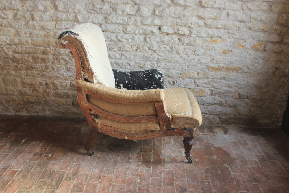 A Victorian deep-seated armchair frame with exposed calico and hessian sub-upholstery, featuring turned timber front legs on brass castors. View II