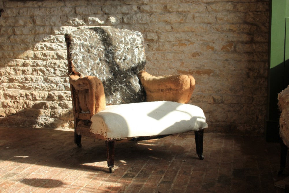 An antique Howard style armchair with exposed calico and horsehair padding, scrolled arms, and turned wooden front legs on brass castors.