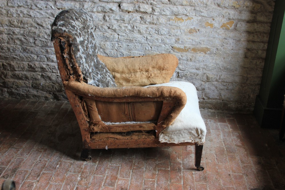 An antique Howard style armchair with exposed calico and horsehair padding, scrolled arms, and turned wooden front legs on brass castors. View II