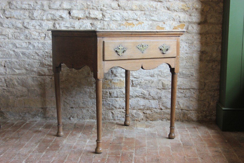 An 18th century pale oak lowboy featuring a single drawer with brass handles, a scalloped apron, and slender turned legs. View II