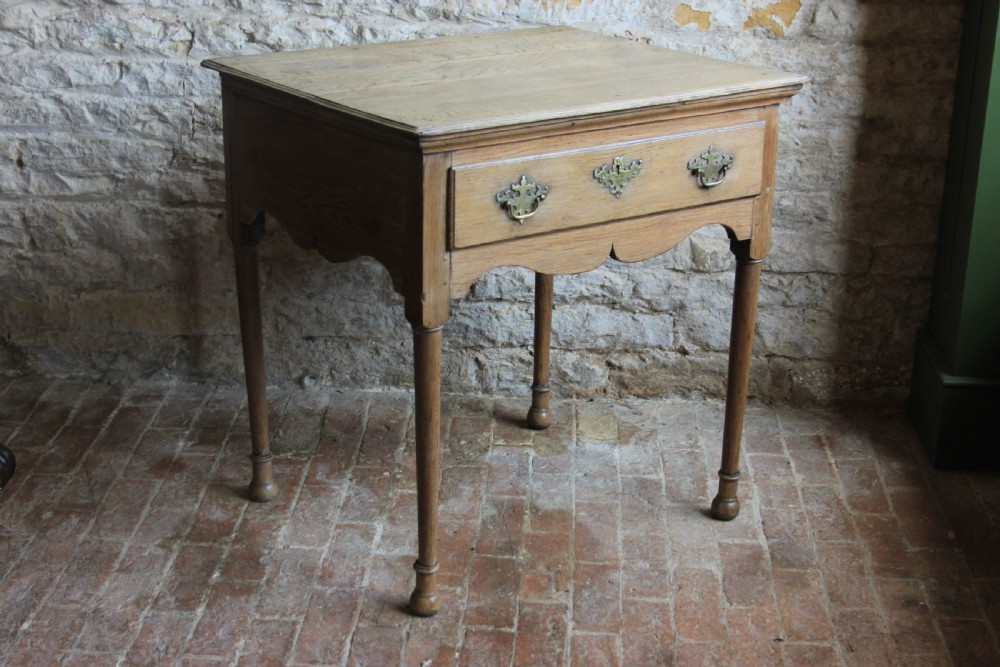 An 18th century pale oak lowboy featuring a single drawer with brass handles, a scalloped apron, and slender turned legs. View III