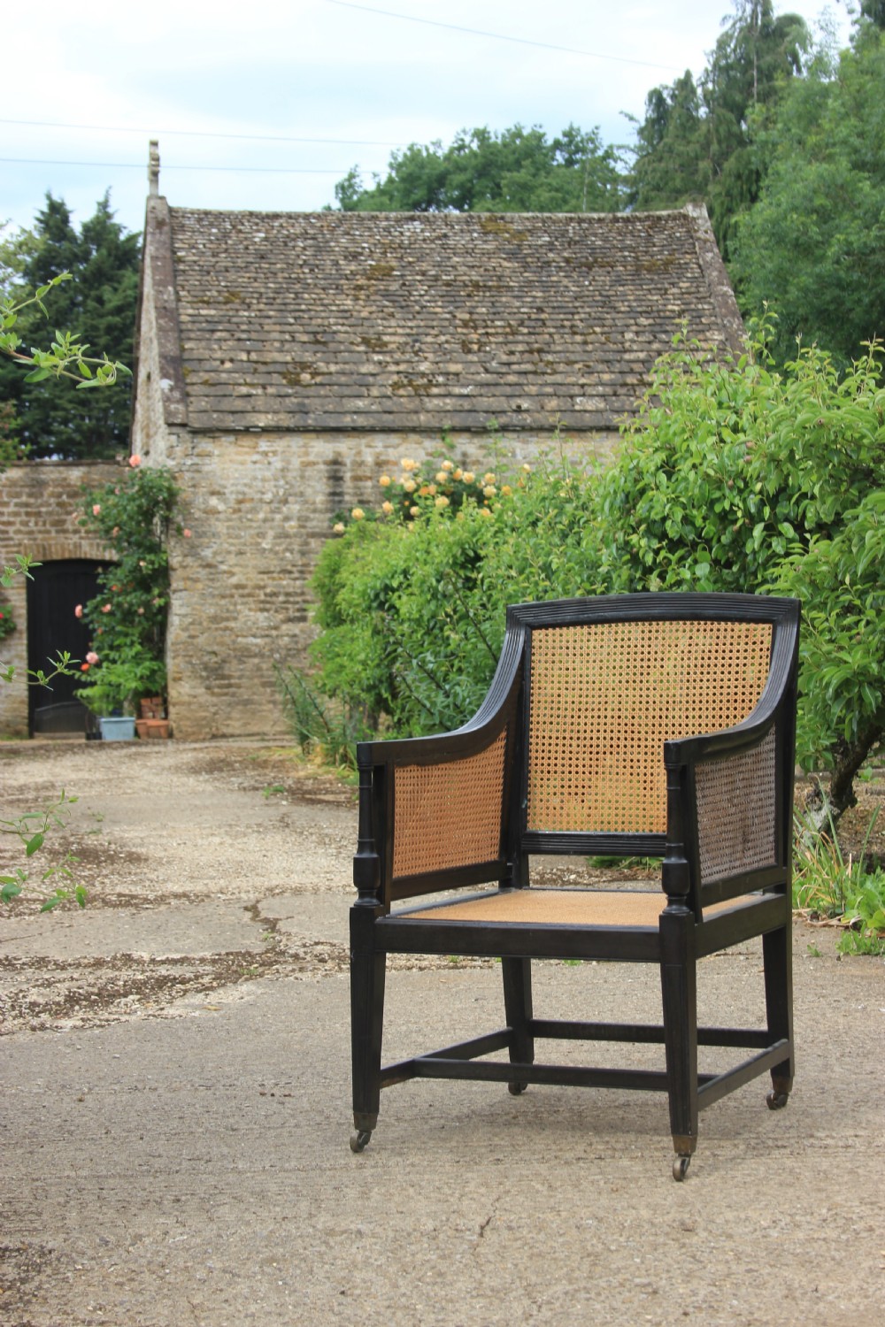 An Anglo-Indian style dark ebony bergere armchair featuring woven cane panelling on the backrest, sides, and seat, resting on straight legs with brass castors.