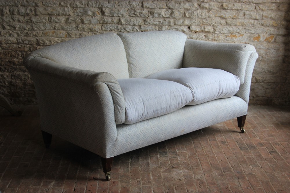 An antique two-seater Howard and Sons Portarlington sofa upholstered in light patterned fabric with deep feather cushions and square legs on brass castors.