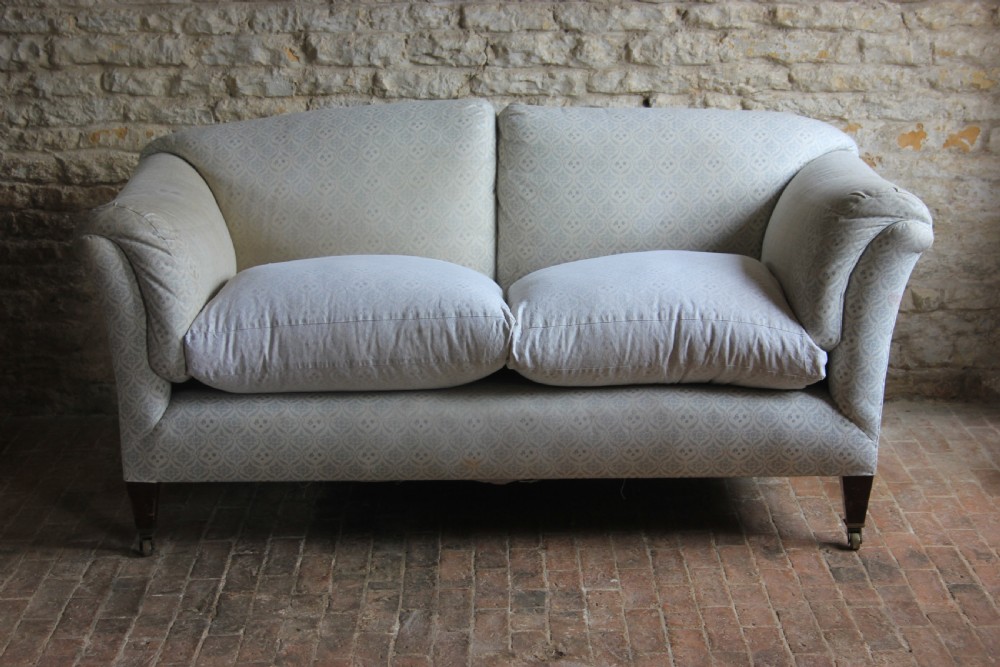 An antique two-seater Howard and Sons Portarlington sofa upholstered in light patterned fabric with deep feather cushions and square legs on brass castors. View II