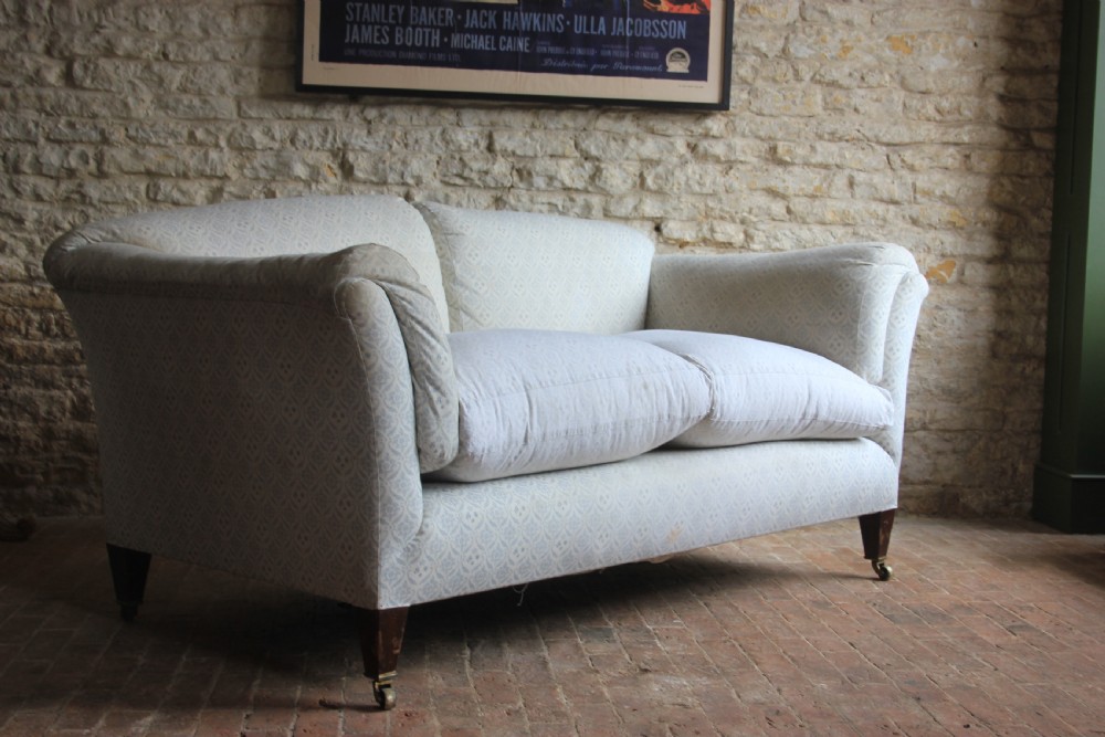 An antique two-seater Howard and Sons Portarlington sofa upholstered in light patterned fabric with deep feather cushions and square legs on brass castors. View IV