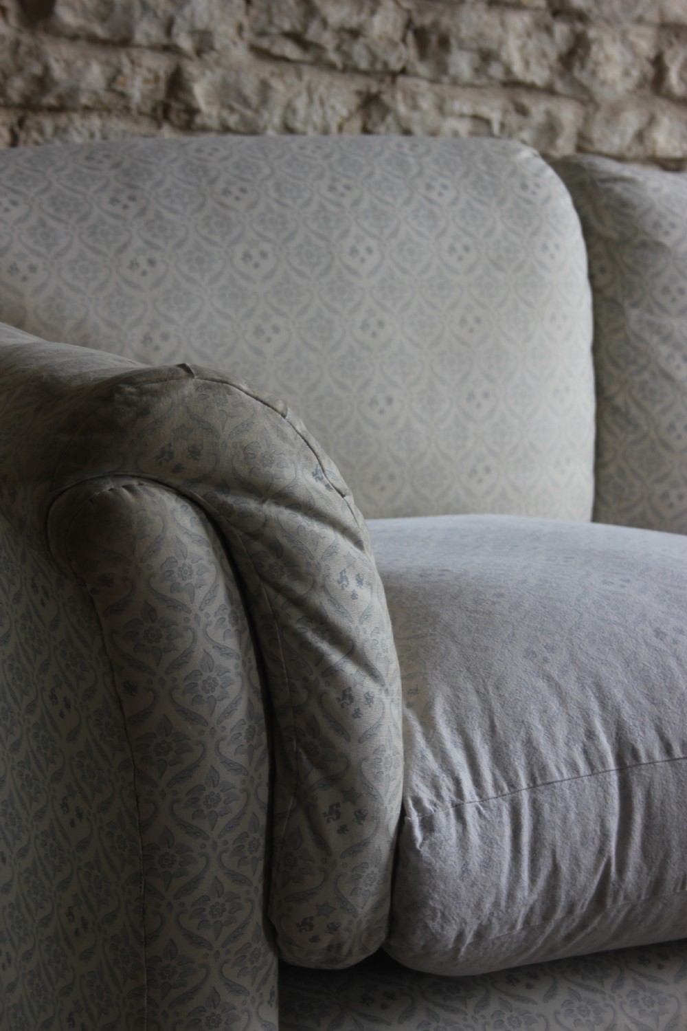 An antique two-seater Howard and Sons Portarlington sofa upholstered in light patterned fabric with deep feather cushions and square legs on brass castors. View V