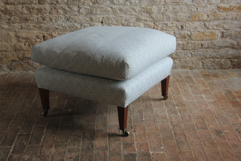 A light blue patterned upholstered Bridgewater armchair paired with a matching rectangular footstool, both raised on tapered mahogany legs with brass castors. View IV