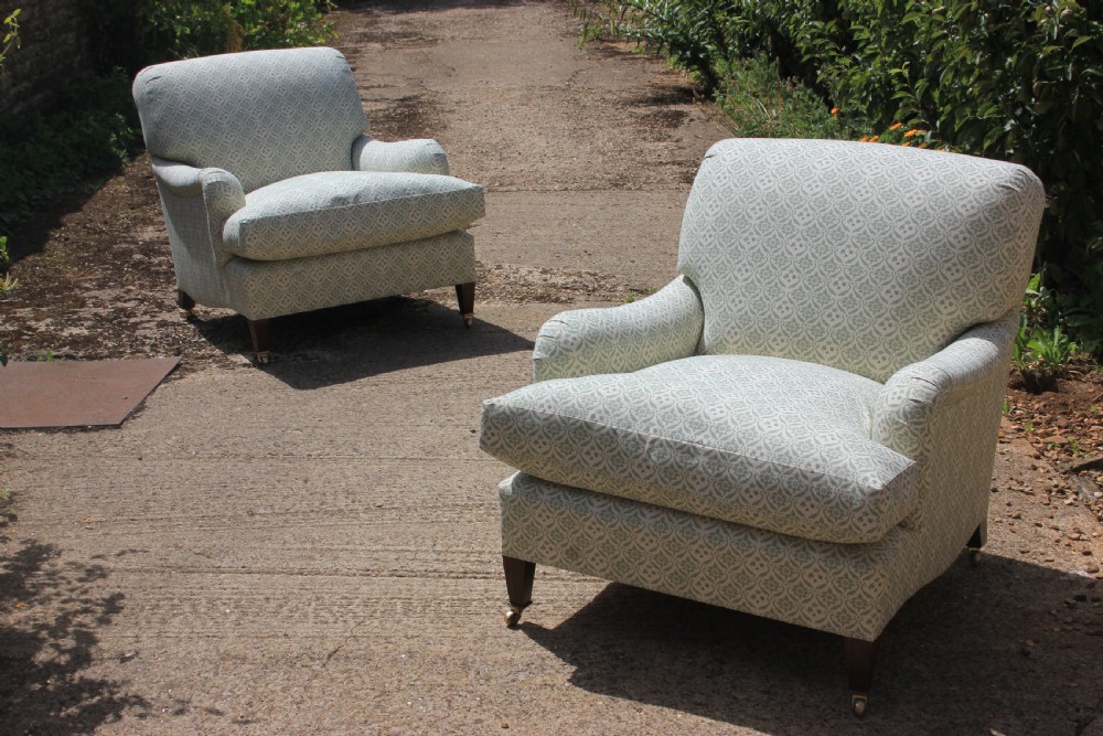 A pair of deep-seated armchairs upholstered in a sage green and off-white patterned fabric with turned front legs on brass castors.