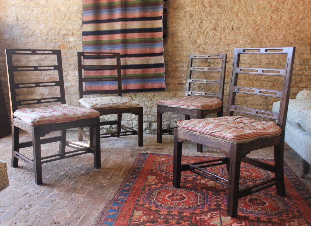 Set of four dark timber 18th-century Irish ladderback dining chairs with slotted horizontal back rails and seat cushions.