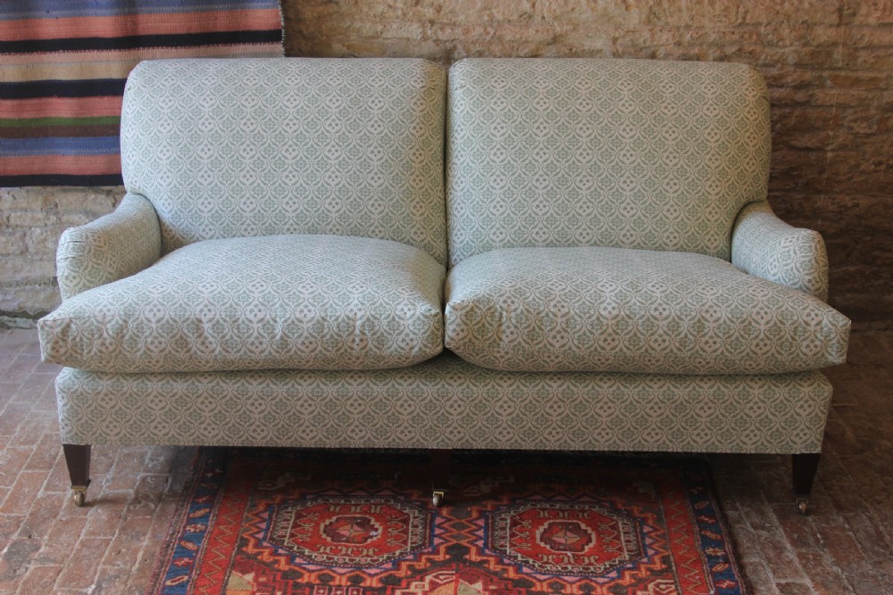 A two-seater Howard and Sons Ivor sofa upholstered in a light green and cream pattern with square tapered mahogany legs and brass castors.