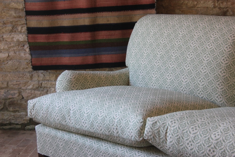 A two-seater Howard and Sons Ivor sofa upholstered in a light green and cream pattern with square tapered mahogany legs and brass castors. View II