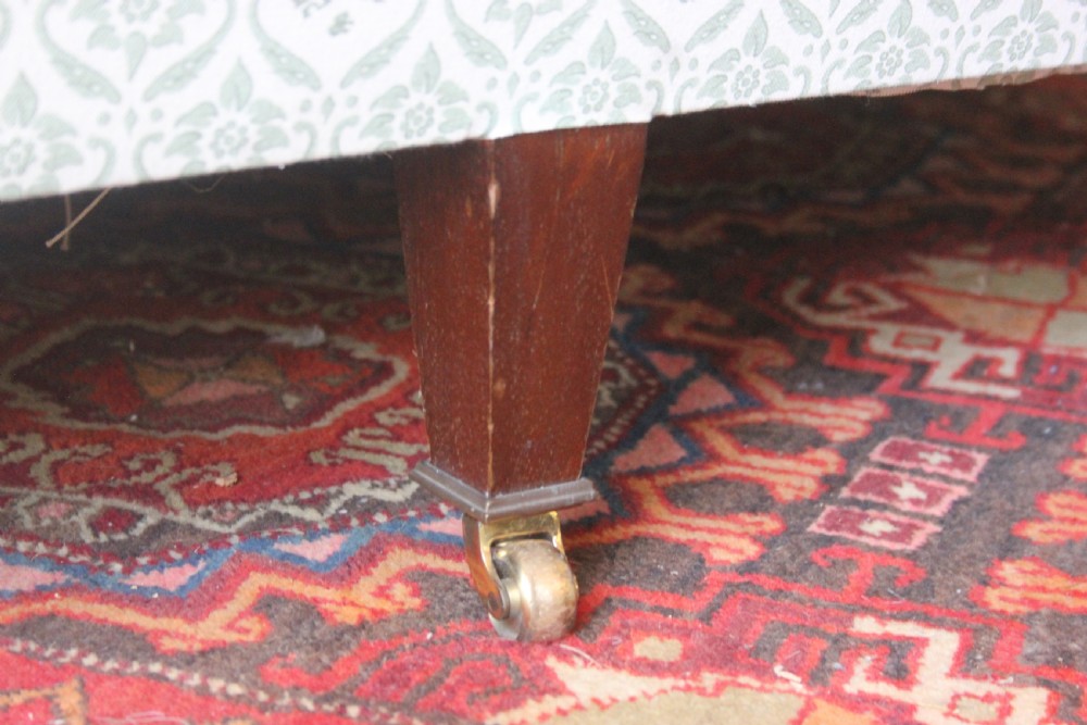A two-seater Howard and Sons Ivor sofa upholstered in a light green and cream pattern with square tapered mahogany legs and brass castors. View III