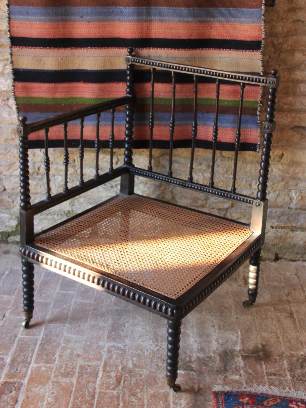 A nineteenth-century dark wood corner armchair featuring bobbin-turned legs and back spindles with a woven cane seat on brass castors.