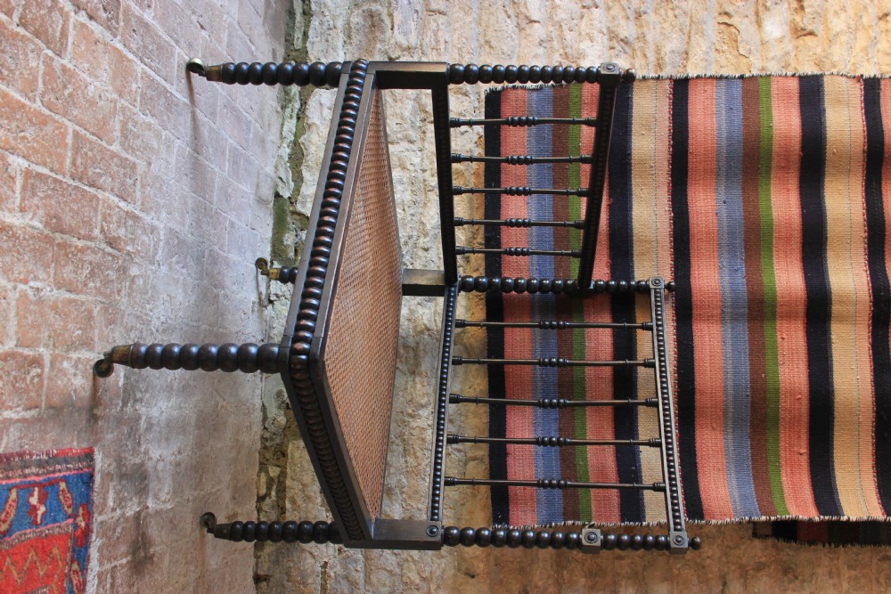 A nineteenth-century dark wood corner armchair featuring bobbin-turned legs and back spindles with a woven cane seat on brass castors. View II