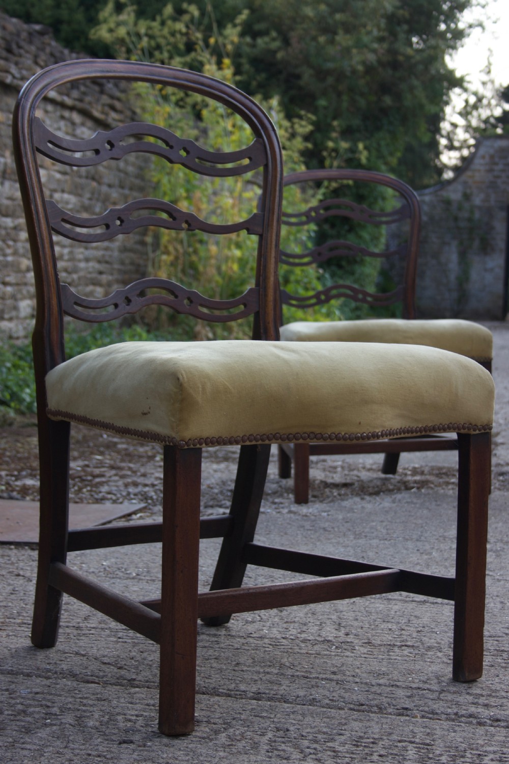 A Georgian dark mahogany dining chair featuring wave-pattern pierced horizontal back rails, a gold velvet upholstered seat with brass studding, and square legs joined by H-stretchers.