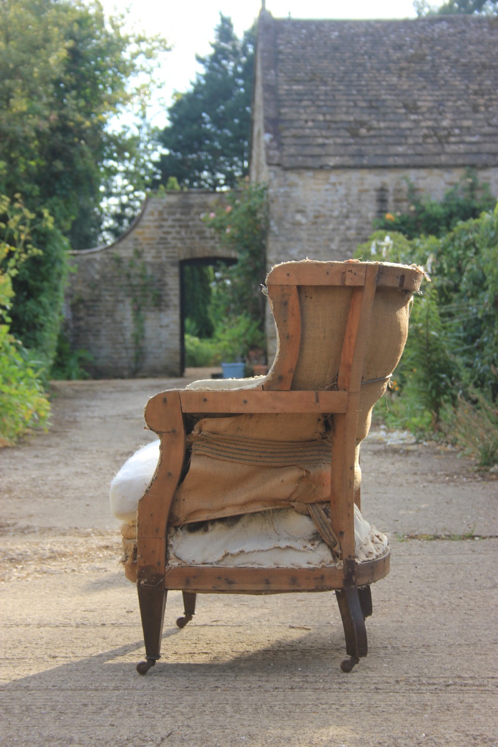 An antique Edwardian barrel back armchair with tapered dark wood legs on castors, featuring exposed hessian lining and a loose seat cushion. View II