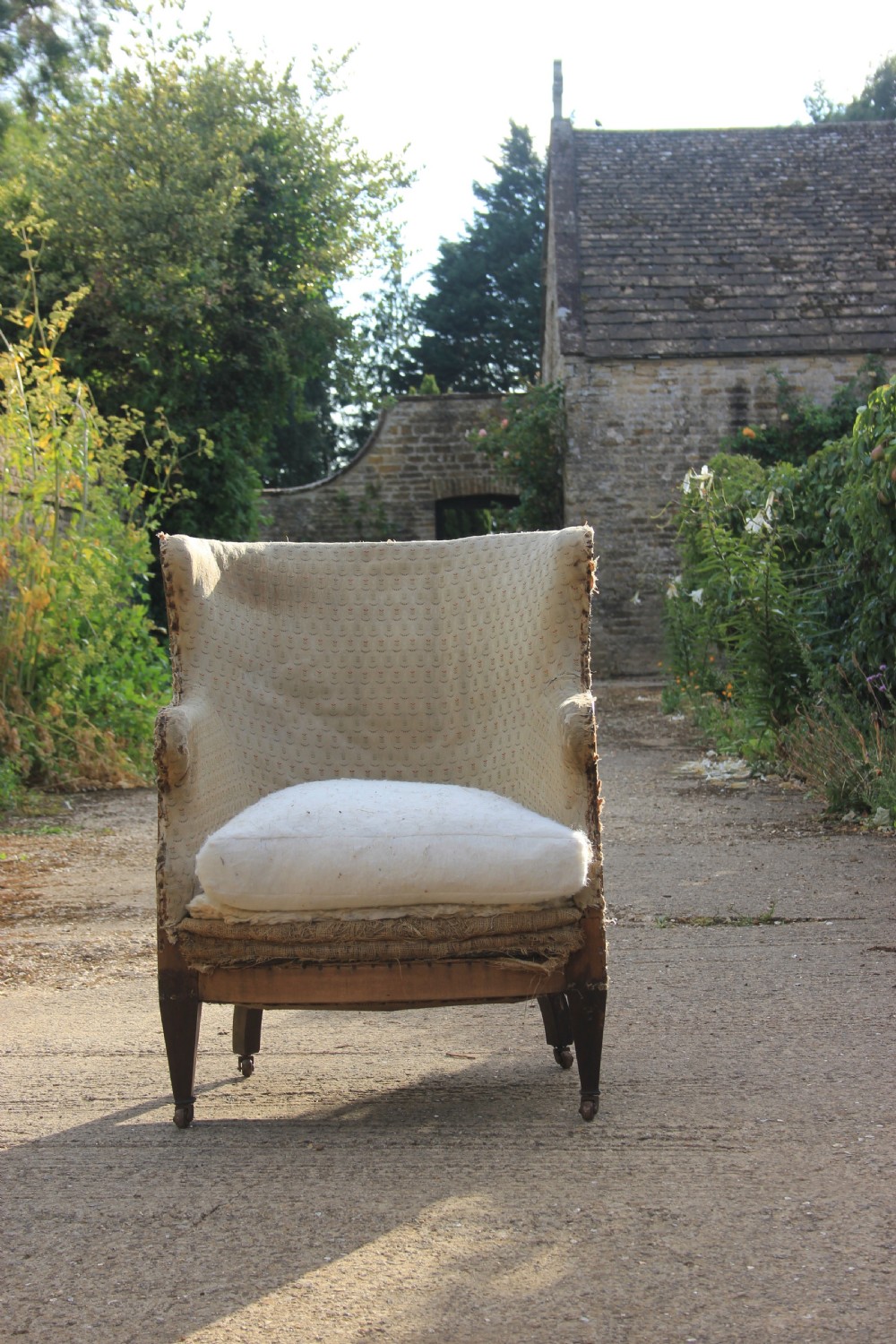 An antique Edwardian barrel back armchair with tapered dark wood legs on castors, featuring exposed hessian lining and a loose seat cushion. View III